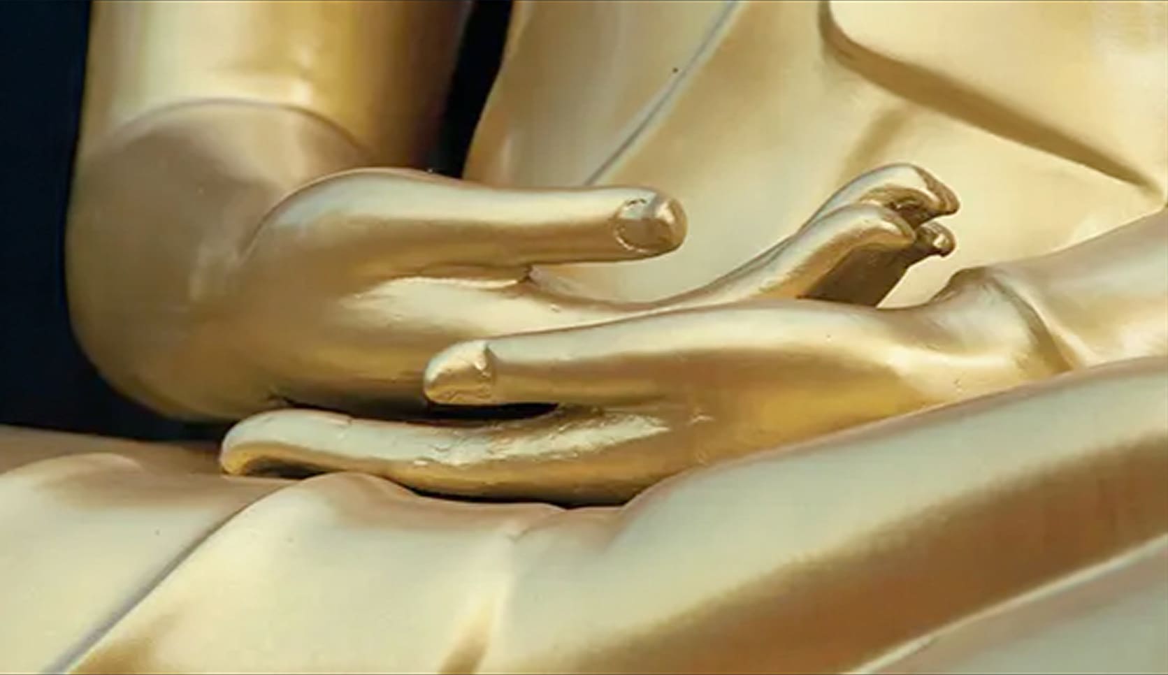 Close-up of a golden Buddha statue's hands in a meditation pose.