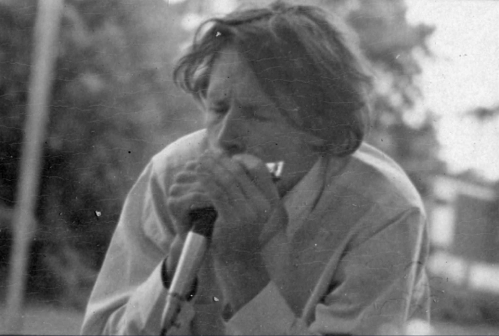Person passionately playing a harmonica into a microphone.